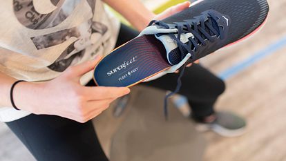 A woman slides a pair of insoles into a shoe.
